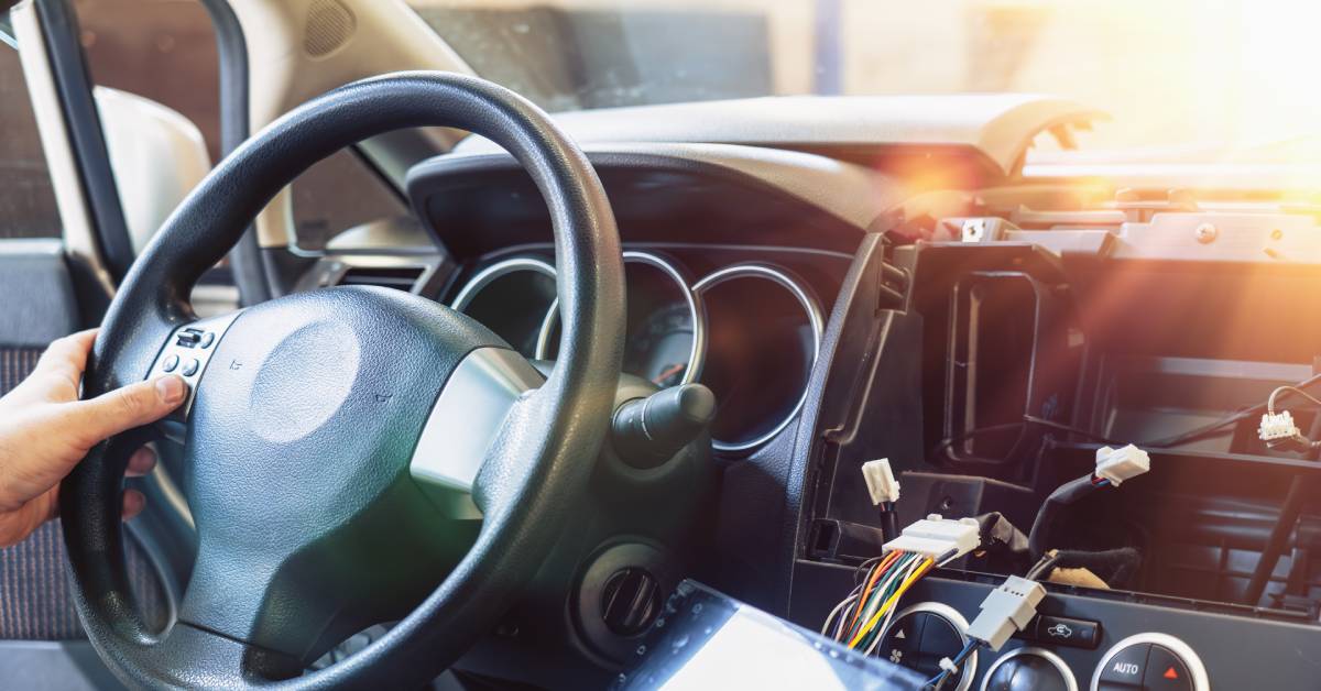 A person testing their car stereo before fulling installing it. The screen is wired to the car and hanging off the dashboard. 