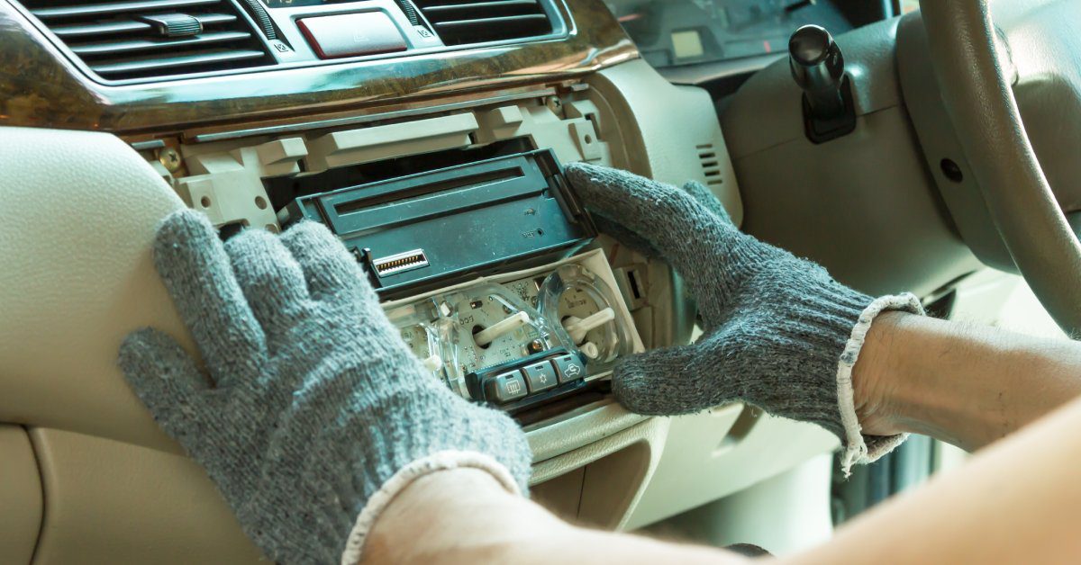 A person positioning a car stereo into a vehicle for installation. They are wearing electricity-resistant gloves.