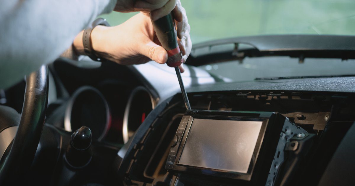 A person installing a car stereo system into a vehicle. They are using a screw driver on the stereo panel.
