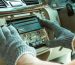 A person positioning a car stereo into a vehicle for installation. They are wearing electricity-resistant gloves.